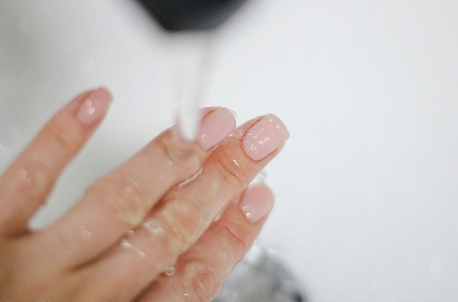 Close-up photo of moisturized fingers with pink-tinted nails against a white background, demonstrating healthy, hydrated skin with a natural sheen. The image illustrates proper skin barrier moisture and care for sensitive skin.